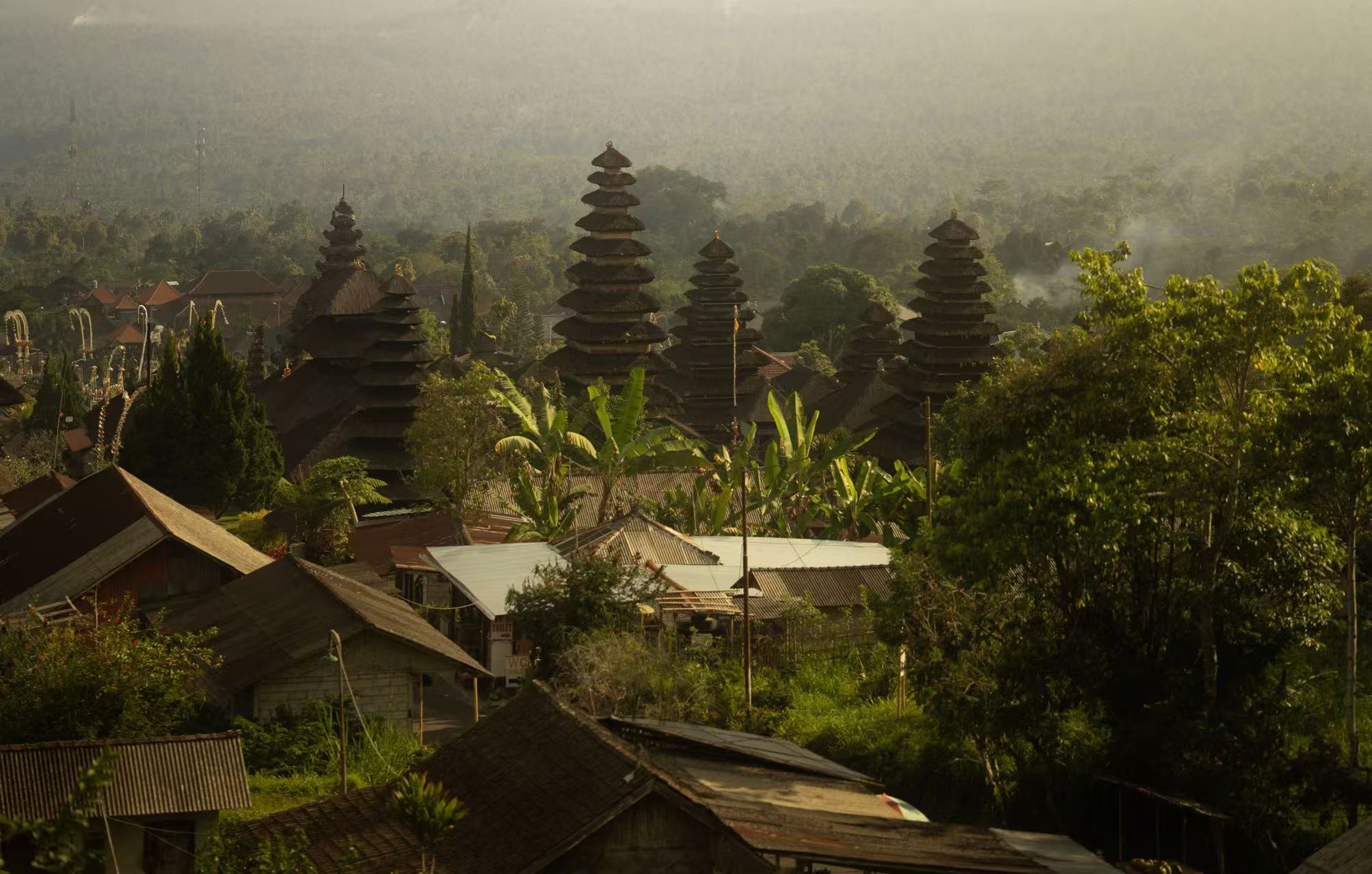 Tiered temple roofs surrounded by lush greenery and misty hills in Indonesia