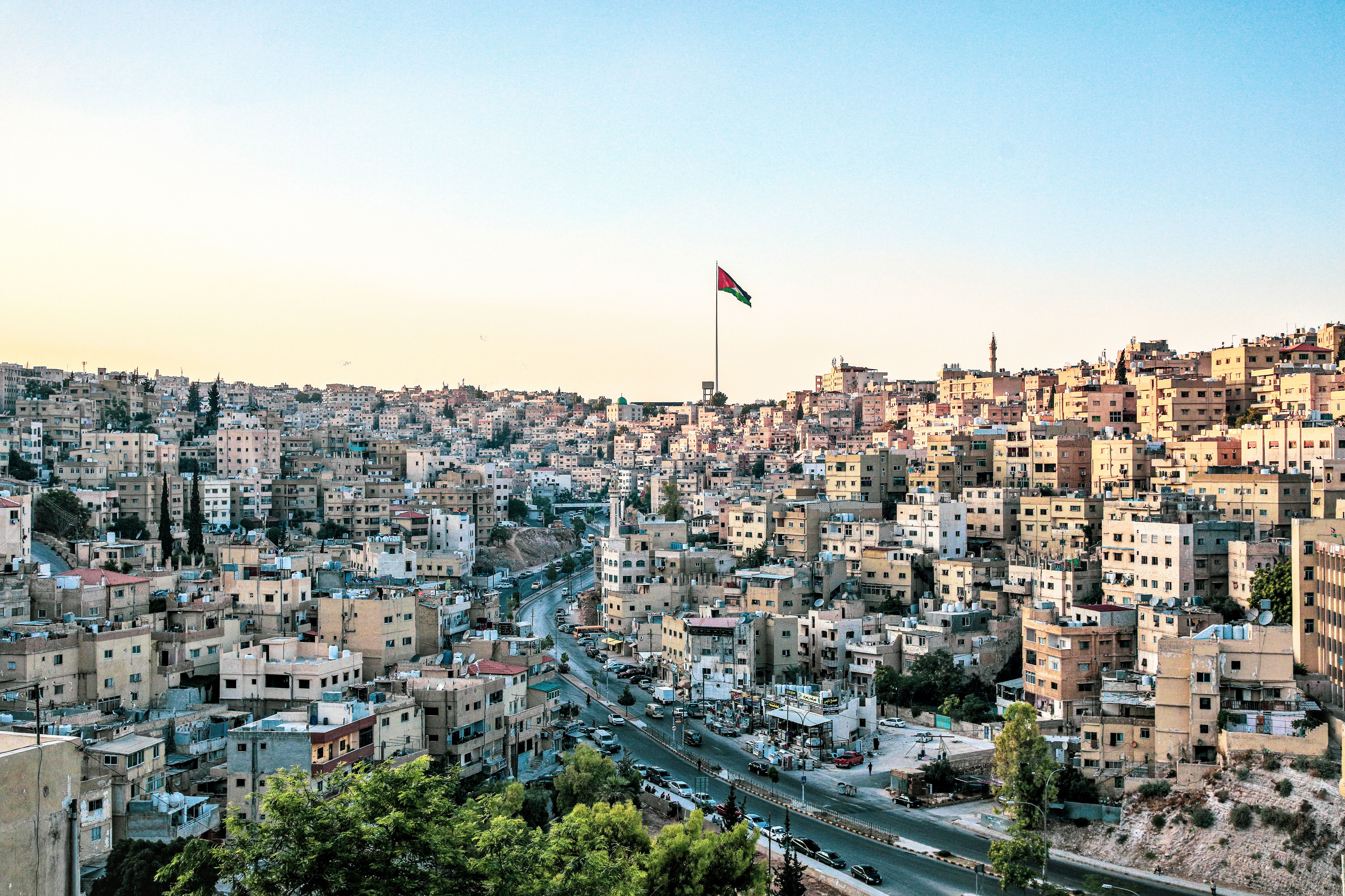 Hillside cityscape with a Jordanian flag above dense buildings and winding streets