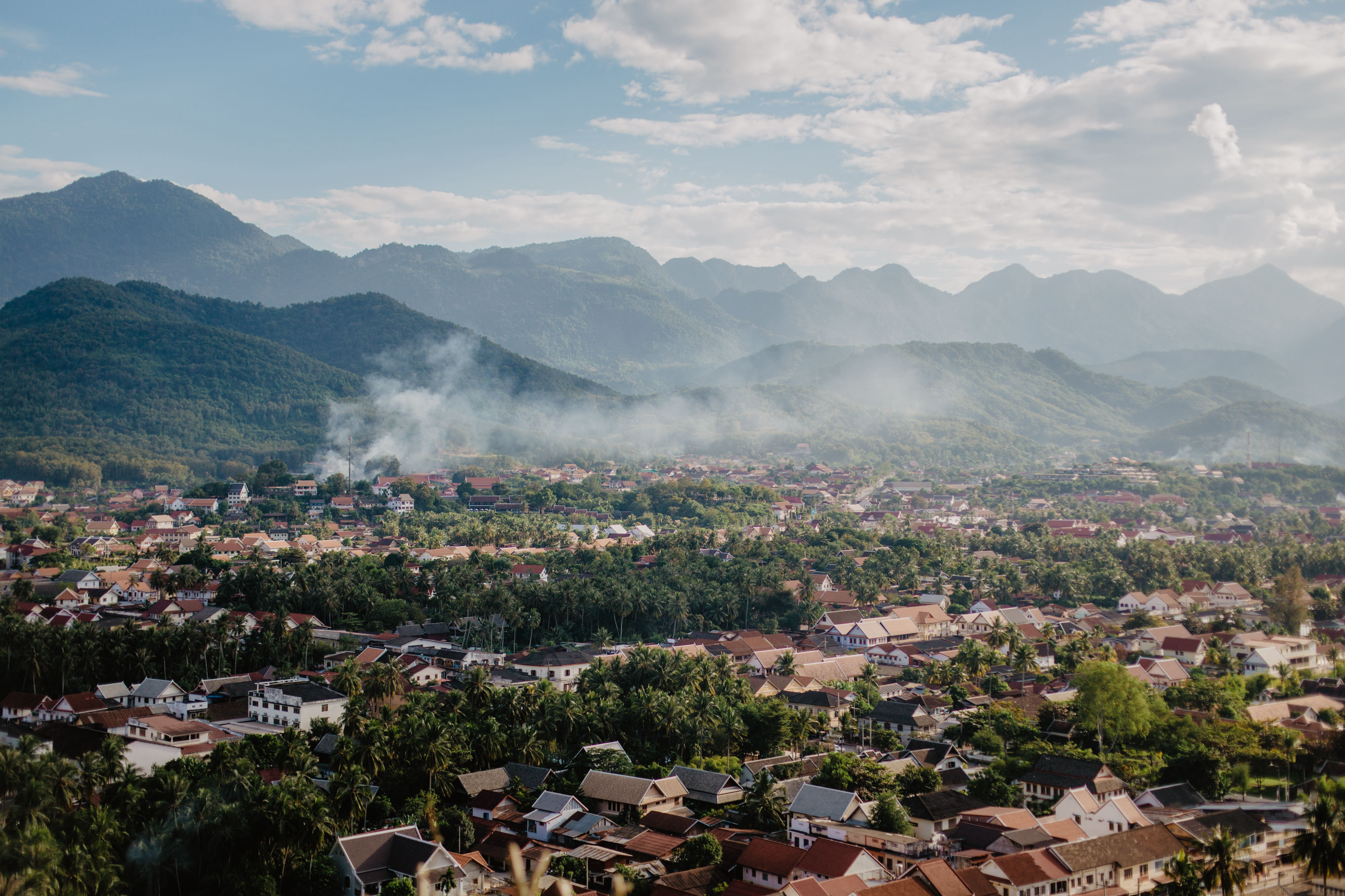 A town surrounded by green mountains beneath a partly cloudy sky in Laos