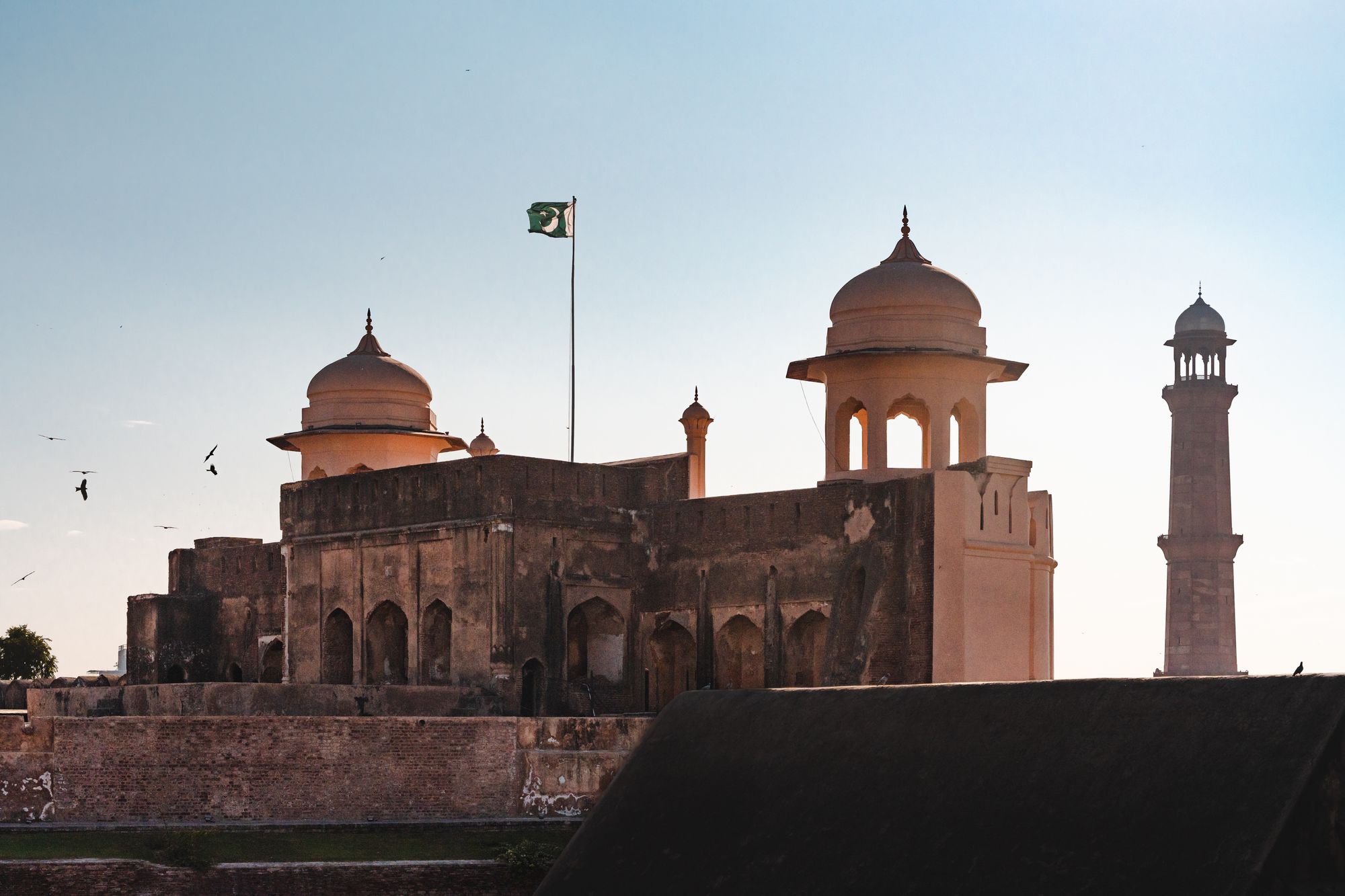 Historic domed architecture and a Pakistani flag under a clear sky